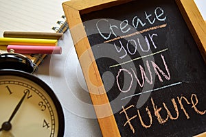 Create your own future on phrase colorful handwritten on chalkboard, alarm clock with motivation and education concepts.