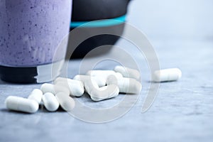 Creatine capsules. Glass of Protein Shake with milk and blueberries and black sporting kettlebell in background. Sport nutrition.