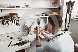 Creating a beauty. Back view of a young male jeweler measuring ring with a tool in workshop.