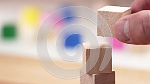 Creating a block toy tower with wooden cubes. The hand sets the top of the tower