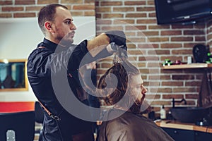 Creating new hair look. Young bearded man getting haircut by hairdresser.