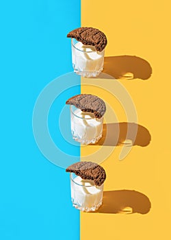 Creative abstract composition made of a glass of milk with a half of brown american cookie on blue and yellow background. Minimal