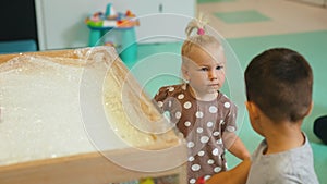 creative activities for kids in kindergarten, little girl and boy painting on the cellophane box with their hands