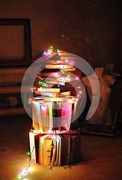 Creative alternative tree of books and colored garlands. Christmas lights. Mannequins, frames in the background.