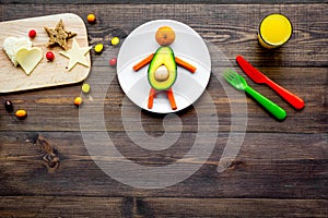 Creative approach to kid`s braekfast. Meal in shape of happy avocado man . Dark wooden background top view copyspace