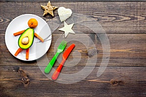 Creative approach to kid`s braekfast. Meal in shape of happy avocado man . Dark wooden background top view copyspace