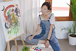 Creative of art concept, Young asian woman hold paint brush and happy to look on art masterpiece