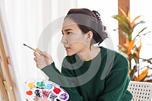 Creative of art concept, Young asian woman hold paintbrush and color palette while looking artwork