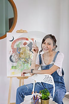 Creative of art concept, Young asian woman hold paintbrush and sitting to rest after drawing finish