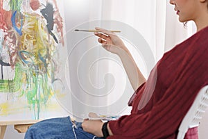 Creative of art concept, Young asian woman sit in studio and hold paintbrush to pointing on artwork