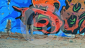 Creative art - teenage boy painting colorful abstract ornament graffiti on street wall with aerosol spray. Slow motion