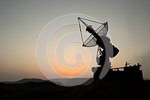 Creative artwork decoration. Silhouette of mobile air defence truck with radar antenna during sunset. Satellite dishes or radio