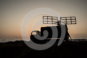 Creative artwork decoration. Silhouette of mobile air defence truck with radar antenna during sunset. Satellite dishes or radio