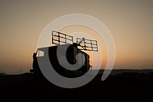 Creative artwork decoration. Silhouette of mobile air defence truck with radar antenna during sunset. Satellite dishes or radio