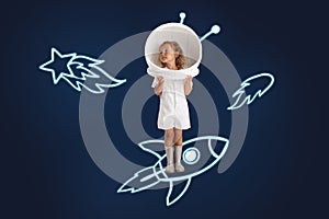 Creative artwork of little girl wearing astronaut helmet and standing on drawn rocket isolated over dark blue background