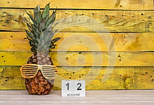 Creative august calendar planner with number 12. Pineapple character on bright yellow summer wooden background with calendar