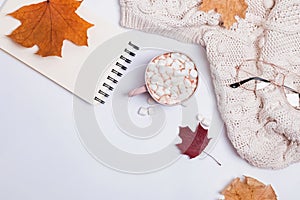 Creative autumn composition with warm knitted sweater, yllow leaves and cocoa with marshmllows