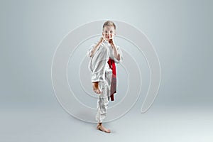 Creative background, a child in a white kimono makes a kick, on a light background. The concept of martial arts, karate