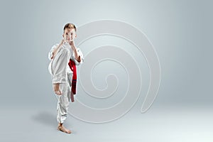 Creative background, a child in a white kimono makes a kick, on a light background. The concept of martial arts, karate