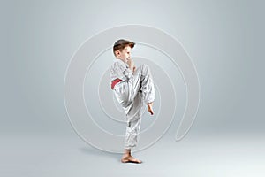 Creative background, a child in a white kimono makes a kick, on a light background. The concept of martial arts, karate