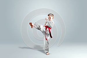 Creative background, a child in a white kimono makes a kick, on a light background. The concept of martial arts, karate