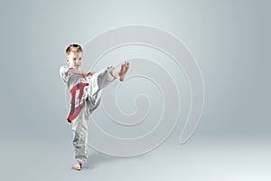 Creative background, a child in a white kimono makes a kick, on a light background. The concept of martial arts, karate