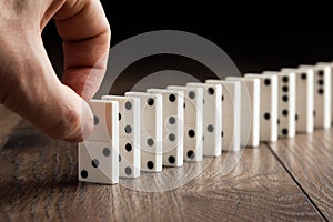 Creative background, Male hand pushing white dominoes, on a brown wooden background. Concept of domino effect, chain