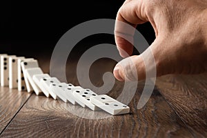 Creative background, Male hand pushing white dominoes, on a brown wooden background. Concept of domino effect, chain