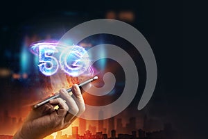 Creative background, a man`s hand holds a phone with a 5G hologram on the background of the city. 5G network concept, high speed