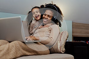 Creative black mother and daughter working on school project, using modern laptop