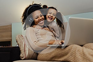 Creative black mother and daughter working on school project, using modern laptop