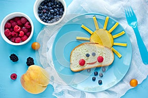 Creative breakfast idea for kids - bread bun with fruit and berry shaped funny cloud with peach sun and blueberry rain , fun with