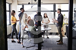 Creative business team in a meeting room listening to an informal presentation, seen from doorway