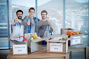 Creative business team standing near donation box and showing thumbs up
