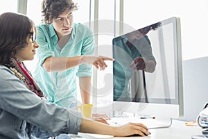 Creative businessman showing something to colleague on desktop computer in office