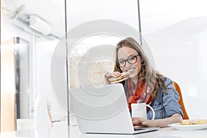 Creative businesswoman having breakfast while working on laptop in office