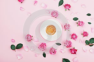 Creative card with coffee cup, green leaves and beautiful pink rose flowers on pastel table top view in flat lay style.