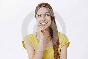Creative charismatic cute happy woman with braid in yellow t-shirt biting finger from curiosity looking right intrigued