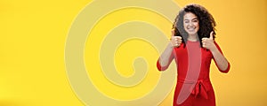 Creative and charismatic happy upbeat woman 25s with curly hair in red dress winking in approval and showing thumbs up