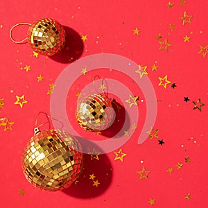 Creative Christmas concept. Shiny gold disco balls over red background. Flat lay, top view. New year baubles, star sparkles. Party