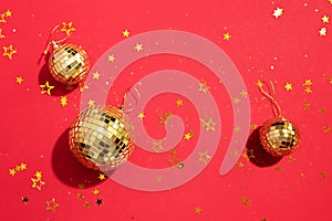 Creative Christmas concept. Shiny gold disco balls over red background. Flat lay, top view. New year baubles, star sparkles. Party