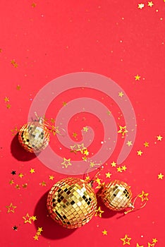 Creative Christmas concept. Shiny gold disco balls over red background. Flat lay, top view. New year baubles, star sparkles. Party