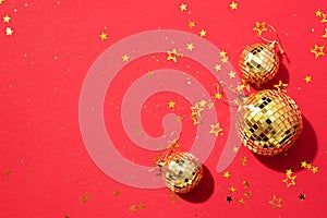 Creative Christmas concept. Shiny gold disco balls over red background. Flat lay, top view. New year baubles, star sparkles. Party