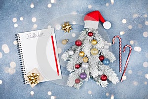 Creative Christmas fir tree decorated Santa hats, gift box and colorful balls with do list on blue background top view. Flat lay.