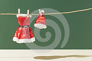 Creative Christmas layout with a clean red Santa Claus suit and hat dries on a rope against a green background. Minimal Xmas or