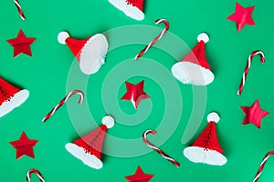 Creative christmas pattern background. Christmas candy canes, red stars and paper santa caps on a green background. New