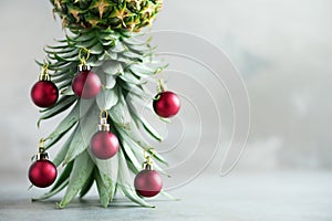 Creative Christmas tree made of pineapple and red bauble on grey concrete background, copy space. Greeting card, decoration for