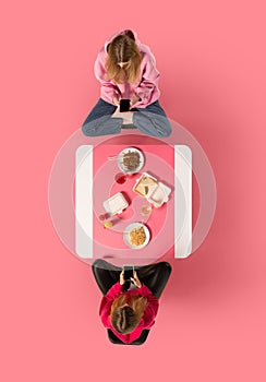 Creative collage. Two young woman, friends sitting at Asian cafe and eating delicious food while speaking against pink