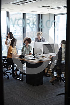 Creative colleagues in working in a casual office, seen through glass wall with text on it, vertical