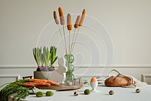 Creative composition of dinning room interior with round table, wooden trace, vase with dried flowers, orange carrot, hyacinth,